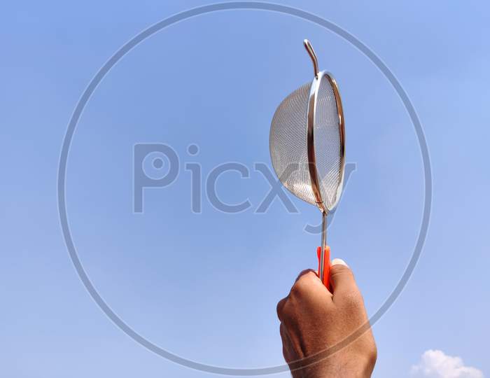 Side View Of South Indian Man Holding Stainless Strainer Or Liquid Filter. Cloud Background