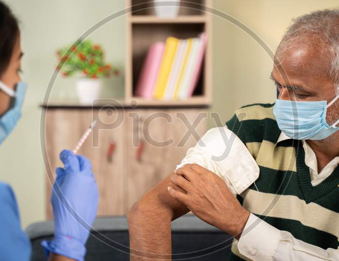 After Doctor Giving Vaccination Shot To Elderly Patient By Syringe Or Injunction, Patient Rubbing His Shoulder At Home - Concept Of Home Health Check To Seniors During Coronavirus Covid-19 Vaccination