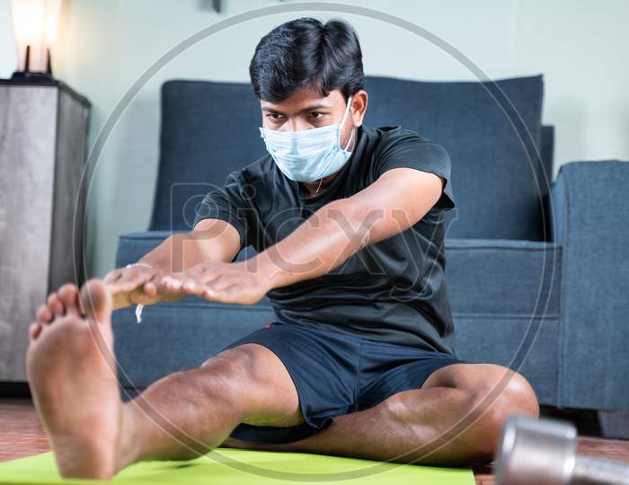 Young Man With Face Mask Busy In Work Out Or Doing Stretching Exercise At Home - Concept Of New Normal, Home Gym Due To Coronavirus Covid-19 Outbreak.