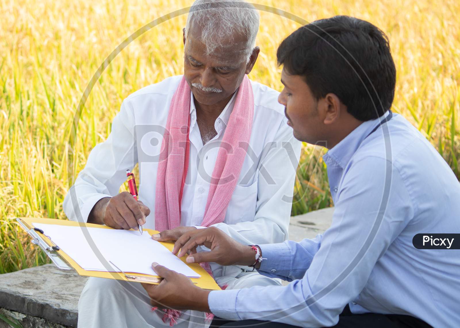 Selective Focus On Farmer, Banker Or Corporate Officer Getting Sign From Farmer While Sitting Near The Farmland - Concept Of Cotract Farming, Business Deal And Farm Loan Approval.