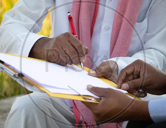 Selective Focus On Farmer Hands, Close Up Of Farmer Hands Signing On Documents While Sitting Near The Farmland - Concept Of Cotract Farming, Business Deal And Farm Loan Approval.