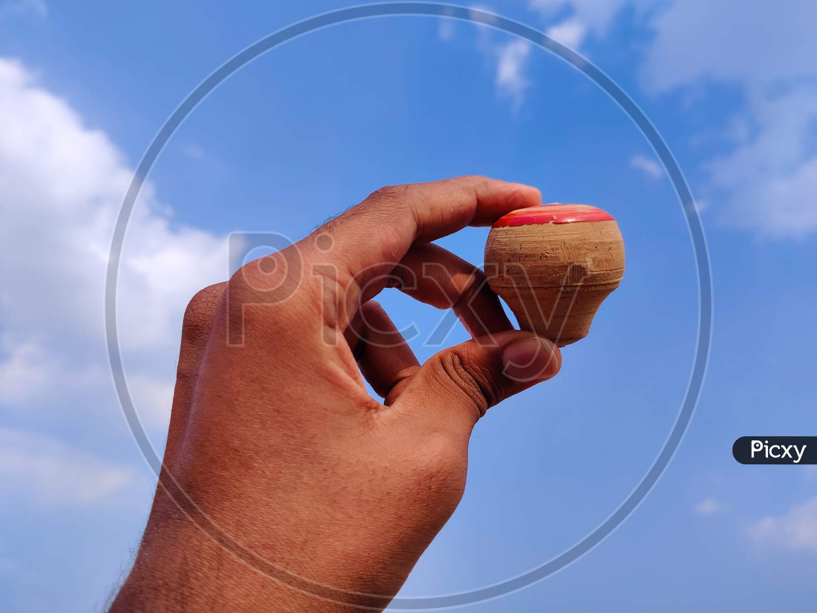 South Indian Man Hand Holding Wooden Spinning Top. Cloud Background