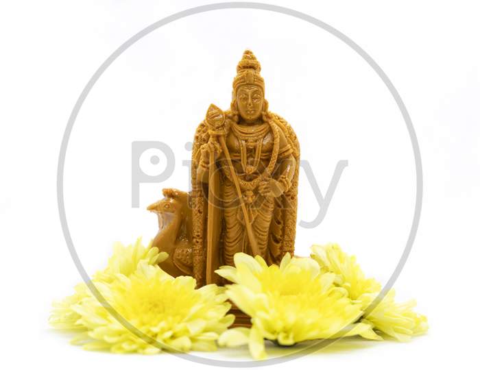 The Wooden Statue Of Lord Murugan With Yellow Flowers Is Isolated On A White Background