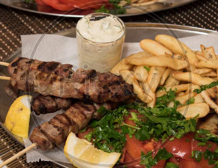 Fried Souvlaki With Greek Salad, Potatoes And Tzatziki Sauce In Plate