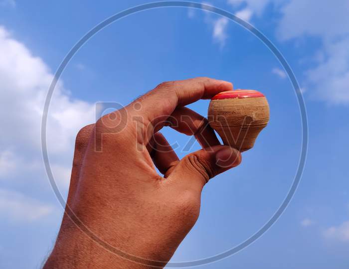 South Indian Man Hand Holding Wooden Spinning Top. Cloud Background
