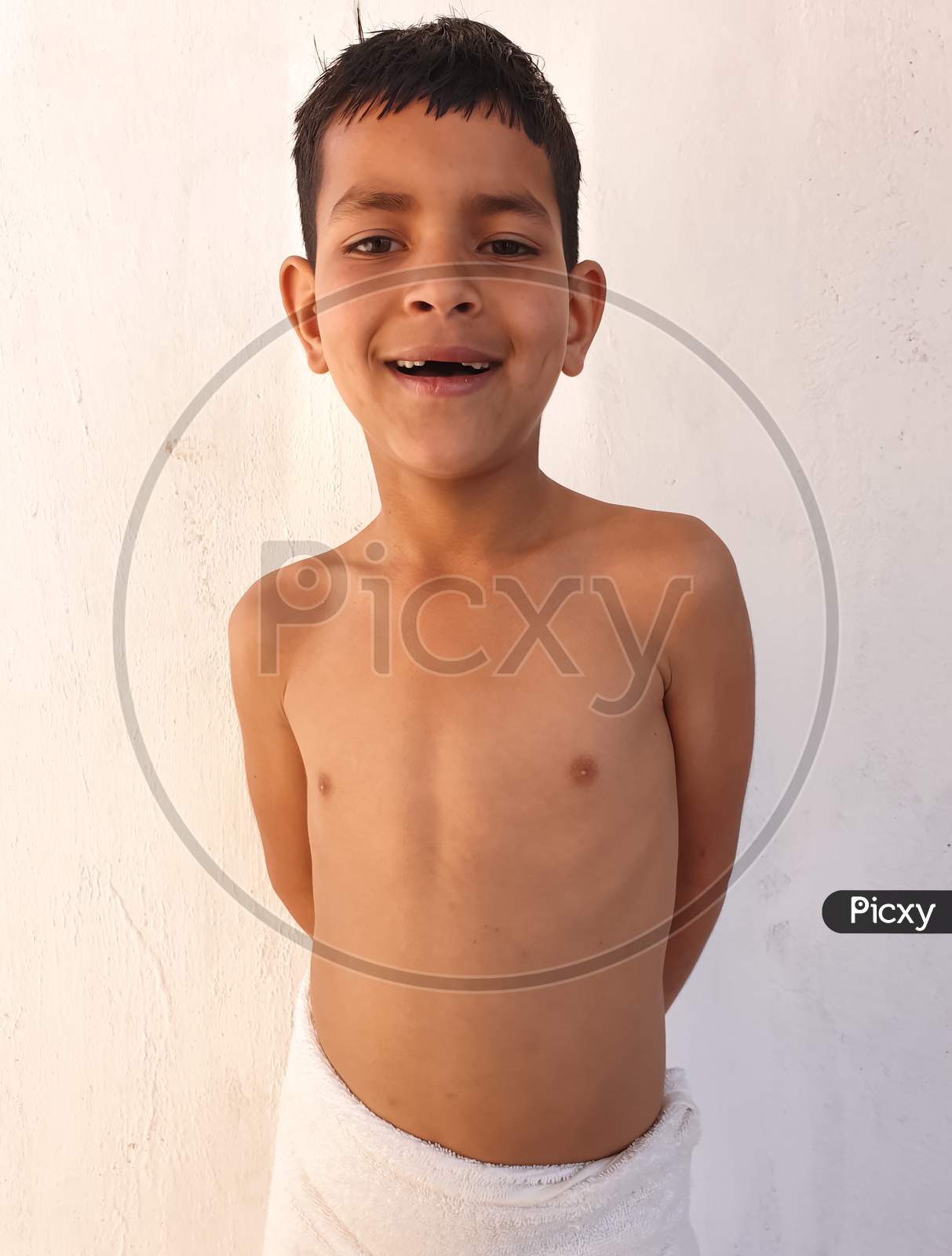 Portrait of a Indian little boy smiling with showing his broken teeth, Shirtless small boy  with wearing white towel, A asian kid looking at camera