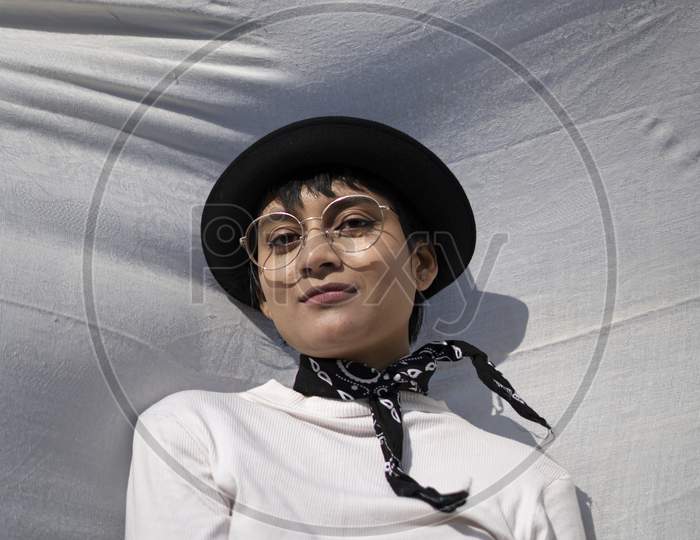 Beautiful Portrait Of An Indian Girl Wearing White Dress And A Black Hat With A Black Hanky On Tied Her Neck, Captured On A White Cloth With Scenery In Background.