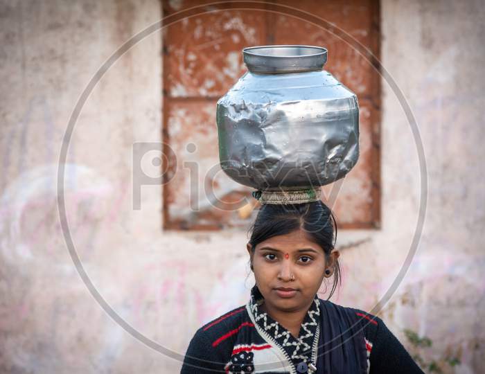 TIKAMGARH, MADHYA PRADESH, INDIA - JANUARY 23, 2021: An unidentified indian village girl carry water on their heads in traditional pots from well, An Indian rural scene.