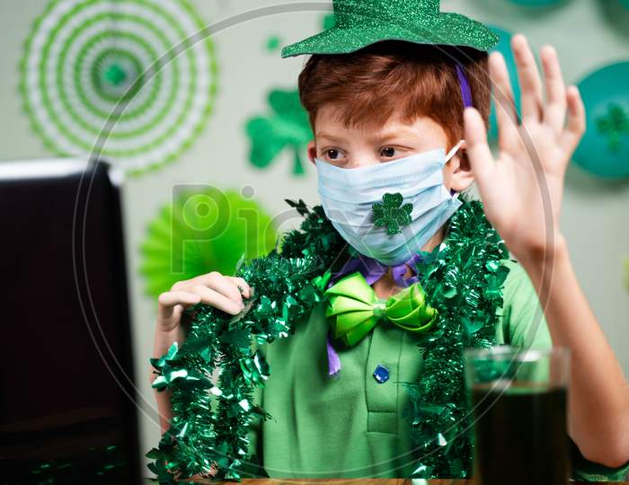 Young Kid With Face Mask Busy In Video Call On Laptop - Concept Of Distant Saint Patricks Day Celebration Due To Coronavirus Or Covid-19 Pandemic.