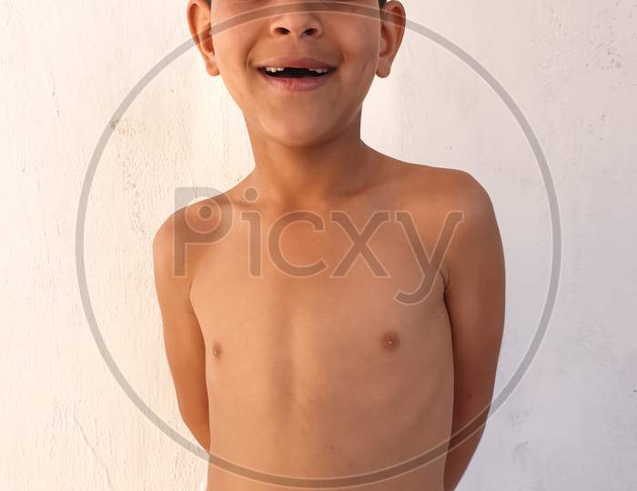 Portrait of a Indian little boy smiling with showing his broken teeth, Shirtless small boy  with wearing white towel, A asian kid looking at camera