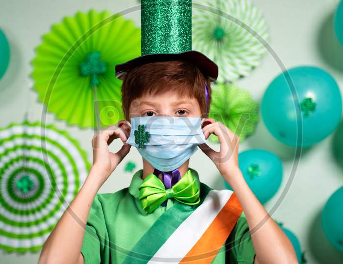Portrait Of Young Kid Wearing Medical Face Mask With Shamrock Sticker As Coronavirus Covid-19 Safety Measures During Saint Patricks Day Festival Celebration.
