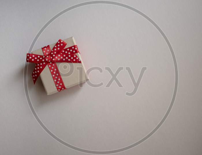 A Small Gift Box With Tied Decorative Bow And Red Ribbon