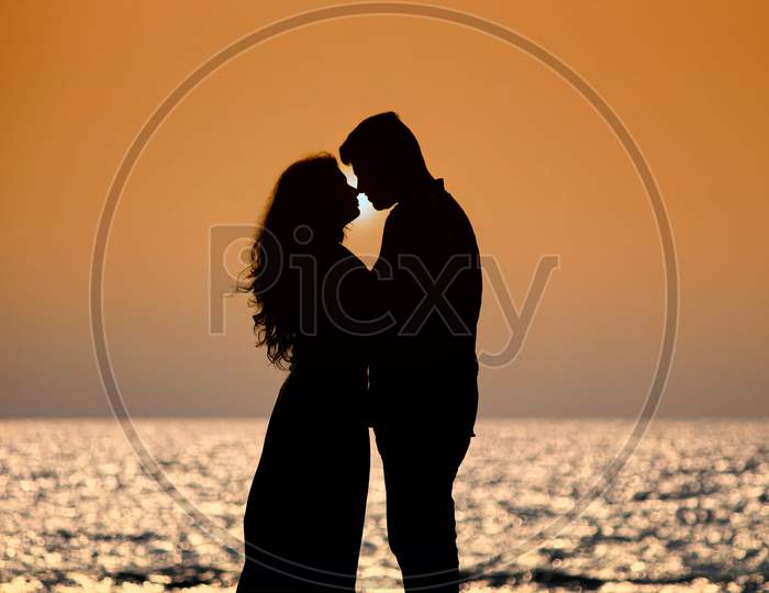 Silhouette romantic couple lovers hug and kiss at colorful sunset on background