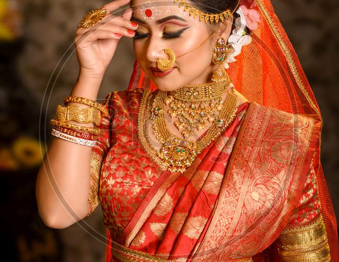 Portrait Of Very Beautiful Indian Bride Holding Betel Leaf, Bengali Bride In Traditional Wedding Saree With Makeup And Heavy Jewellery In Studio Lighting Indoor