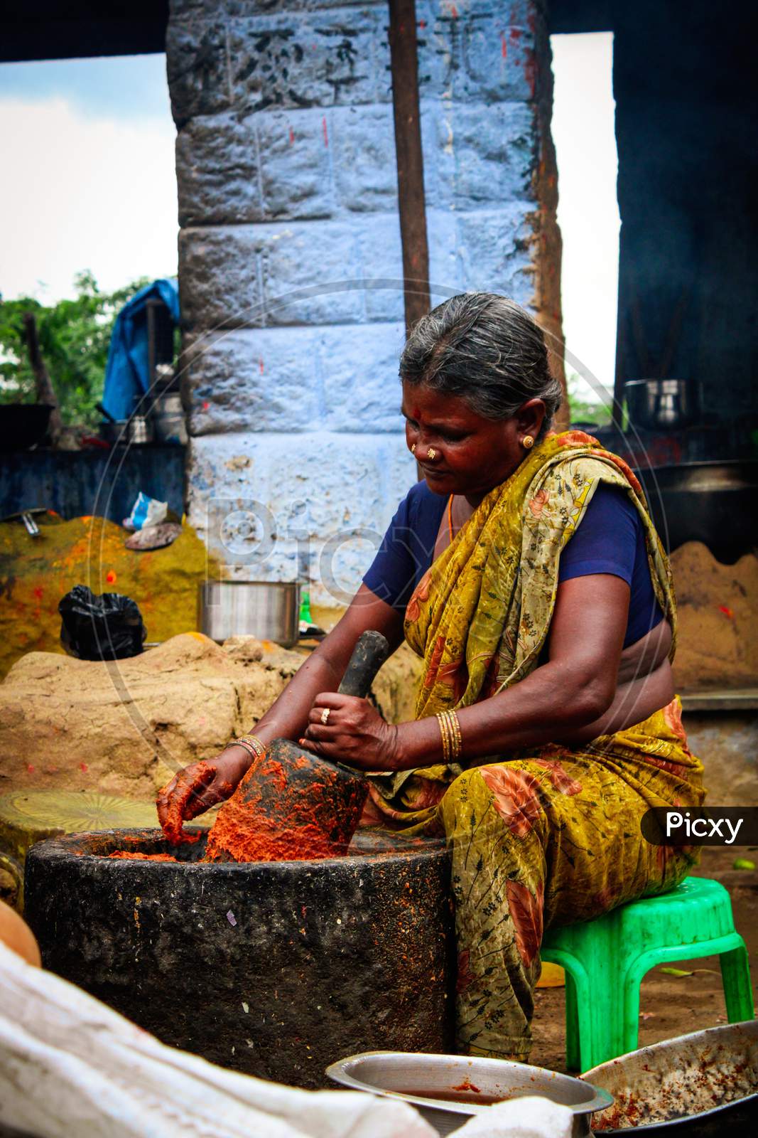 Indian Women powdering spices in big stone bowl