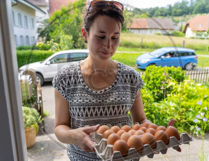 Delivery Of Fresh Eggs At The House Door By A Young Smiling Woman.