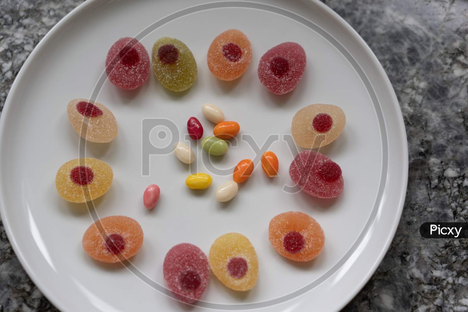 Sweeties For Easter. Easter Candies In A Circle On A White Plate On A Gray Granite Table.