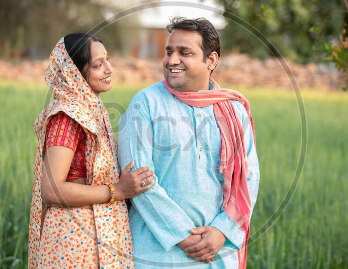 Happy Indian Rural Farmer Couple In Agricultural Field Looking At Each Other Laughing.