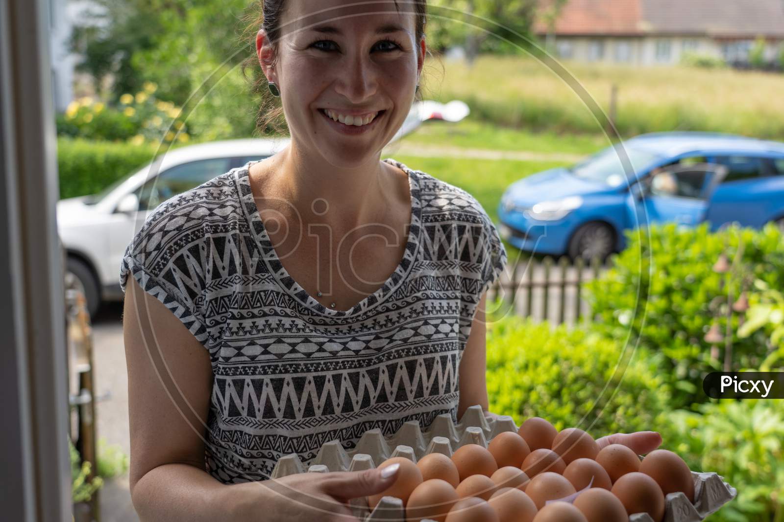 Delivery Of Fresh Eggs At The House Door By A Young Smiling Woman.