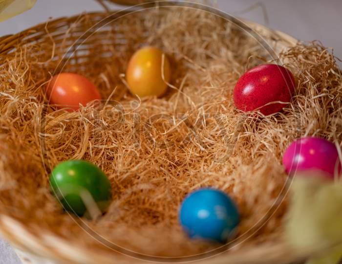 Colored And Cooked Easter Eggs In A Nest Of Straw In Straw Basket On White Ground.