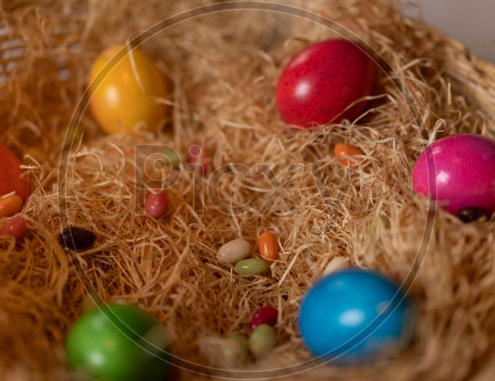 Colorful Cooked Easter Eggs And Candy Eggs In Hay Basket.
