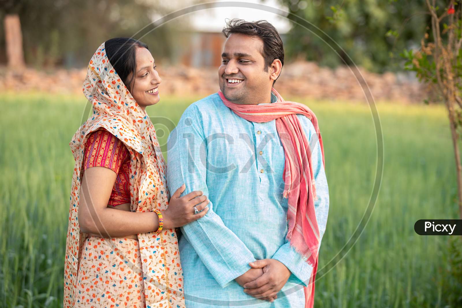 Happy Indian Rural Farmer Couple In Agricultural Field Looking At Each Other Laughing.