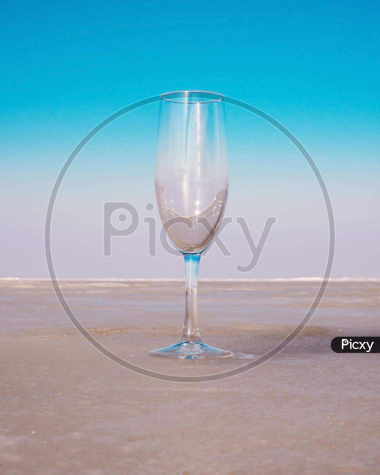 Empty wineglass goblet on beige surface against blue sky background