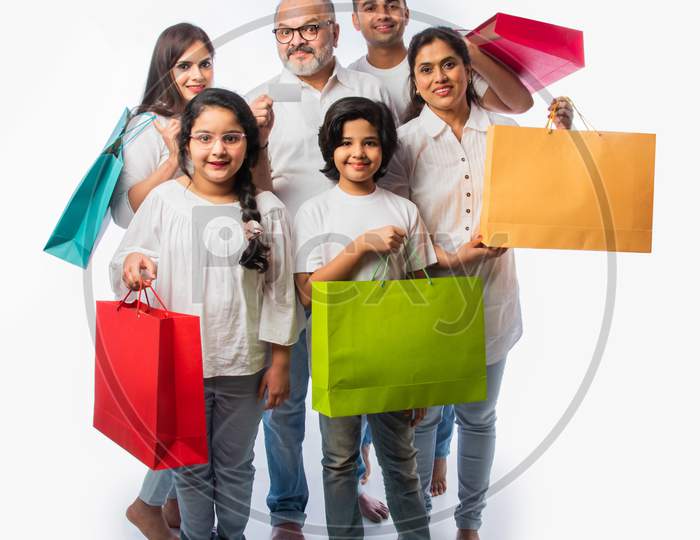 Indian Family With Shopping Bags Includes Young Parents, Grand Parents And Kids Against White