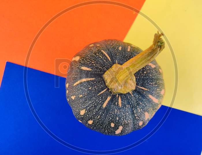 Top View Of Small Sized Green Color Pumpkin Isolated On Blue,Orange,Yellow Background