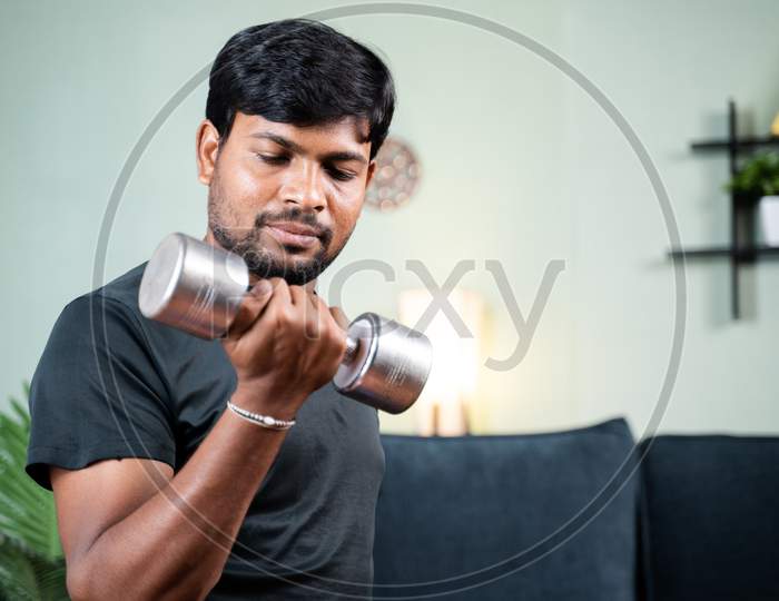 Young Man In Work Out Or Doing Exercise Using Dumbbell At Home - Concept Of Home Gym Due To Coronavirus Covid-19 Lockdown.
