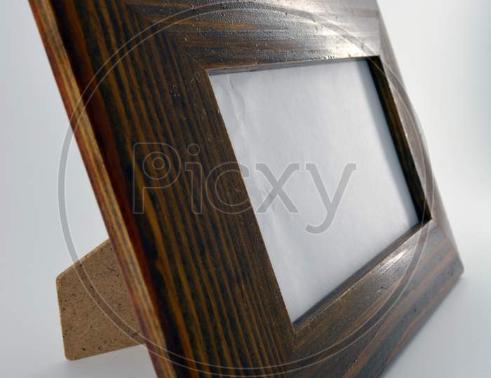 Wooden frame made of natural wood for photos and images covered with reflective varnish and located on a white plastic background.
