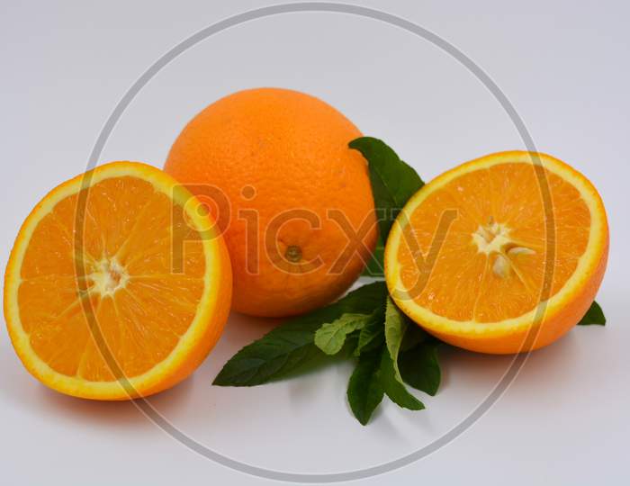 Healthy ripe delicious fruits for human health. Juicy fruits of orange orange with bright green mint. One whole orange and two halves of an orange.