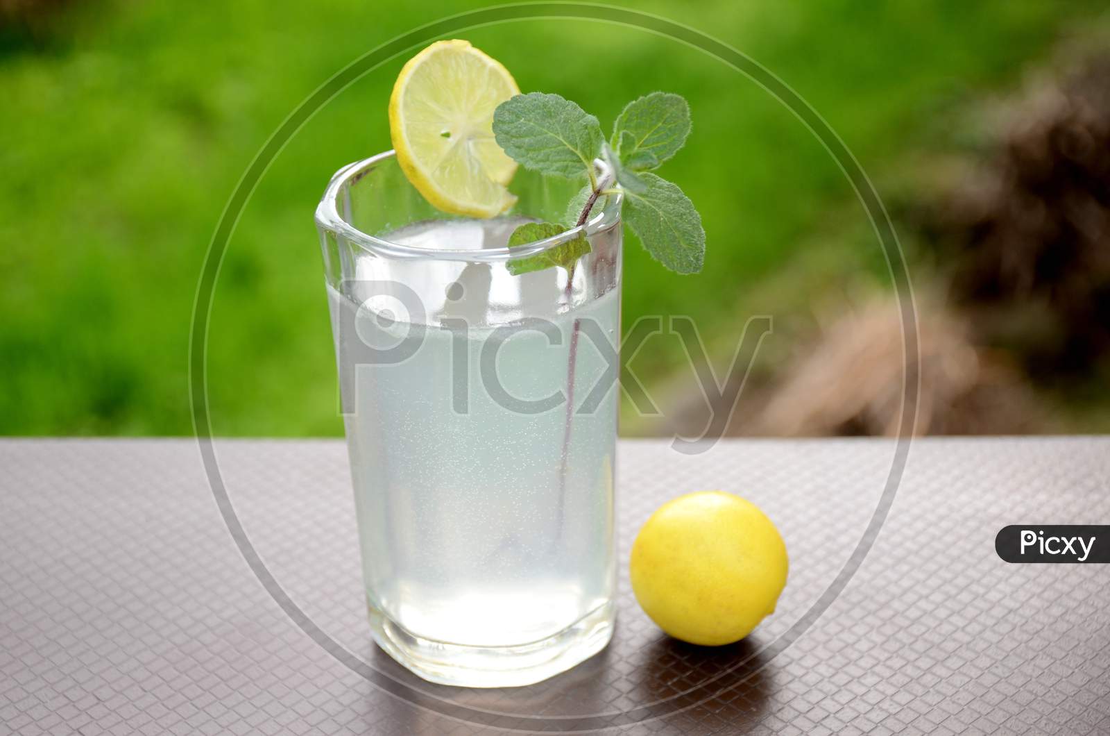 The Fresh Lemon Juice With Green Mint In The Glass And Lemon On The Green Brown Background.
