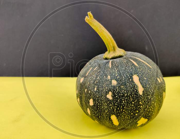 Small Green Cute Pumpkin Isolated On Yellow And Black Background