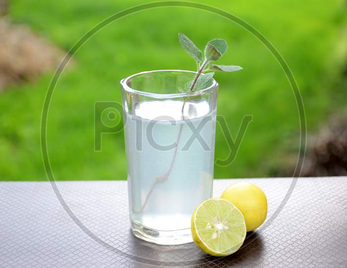 The Fresh Lemon Juice With Green Mint In The Glass And Lemon On The Green Brown Background.