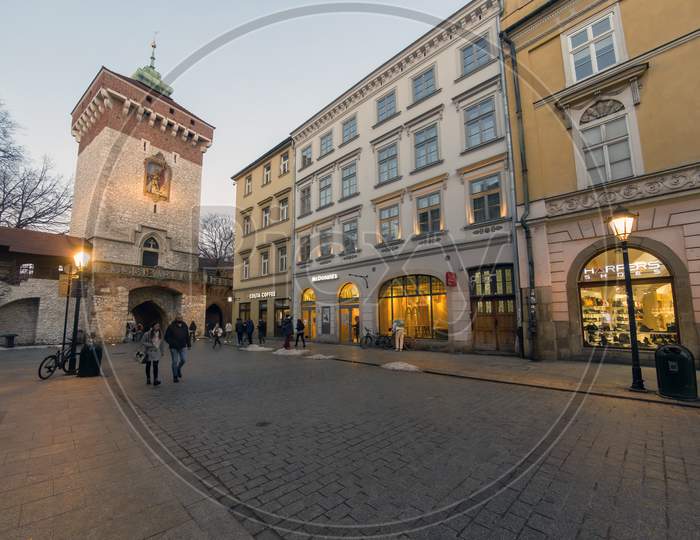 Krakow, Poland - February 20, 2021: Wide Angle Shot Of A European Street And People Taking A Walk During Evening In The Old Town Of Cracow City. People Walking Against Restraunts