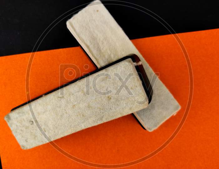 Top View Of Two Plastic Black Board Duster With White Material Pad On Orange Background
