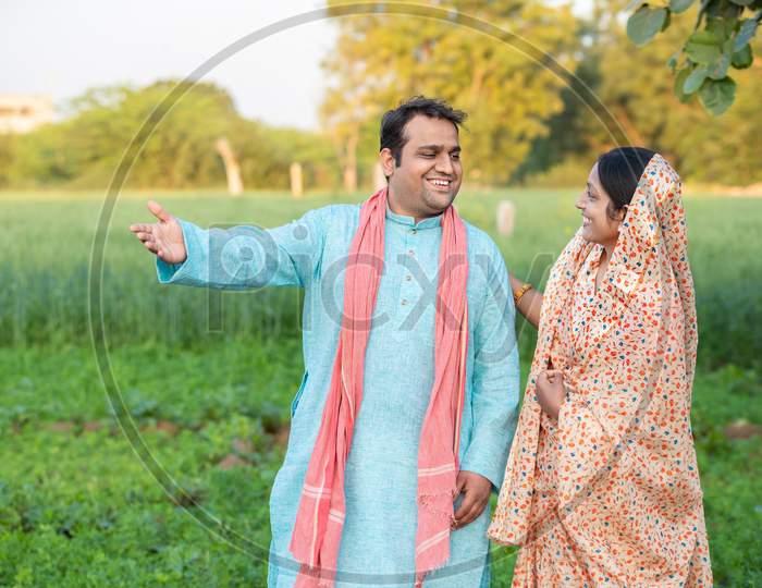 Happy Young Indian Rural Farmer Couple In Agricultural Field Looking At Each Other Laughing.