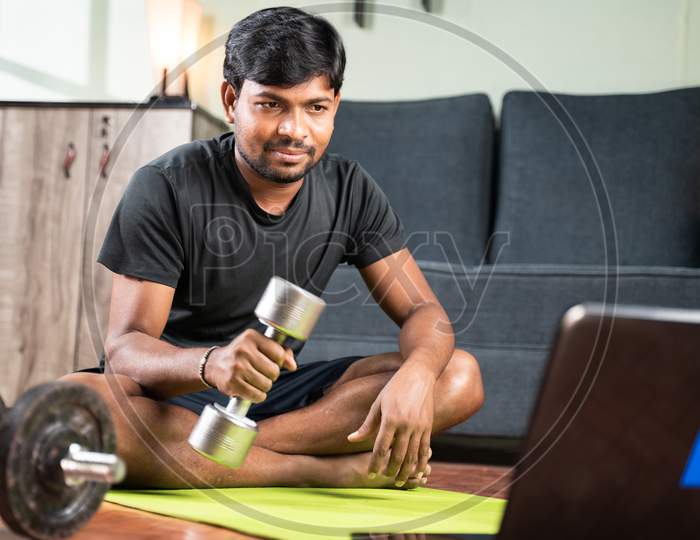 Young Man Busy Learning How To Use Dumbbells Through Online Tutorials By Seeing Laptop At Home - Concept Of Home Gym, Exercise Due To Coronavirus Covid-19 Pandemic.