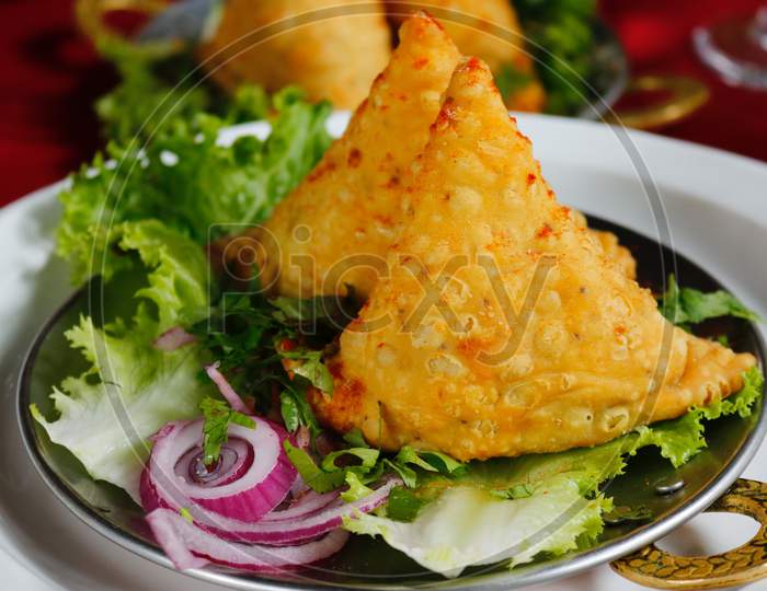 Close-Up Photo of Fried on Saucer -Samosa with Green vegetable & Onion Sliced Served.