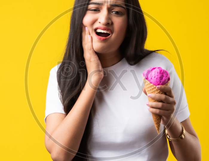Pretty Young Indian Woman With Sensitive Teeth And Eating Cold Ice Cream On Yellow Background