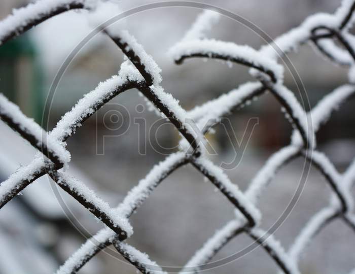 Metallic old rusty netting net decorated with white snow, bright hoarfrost and beautiful snowflakes.