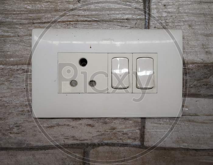 White Switch Board With Two Switch, One Plug And Tiled Background Selectively Focused