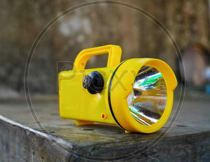 Yellow Electric Led Torch Flashlight With Illuminating Transparent Glass Isolated On A Rough Ground. Suitable For Farmer And Police Use.