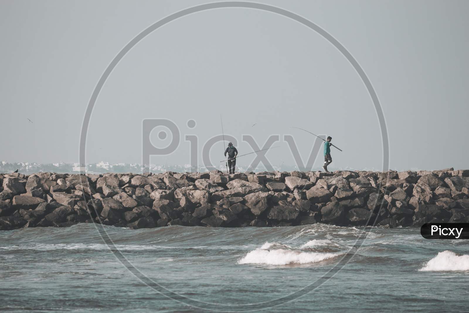 Kovalam, Tamil Nadu, India - February 04 2021: People Fishing Over The Rocks Along The Kovalam Beach, Chennai, India.