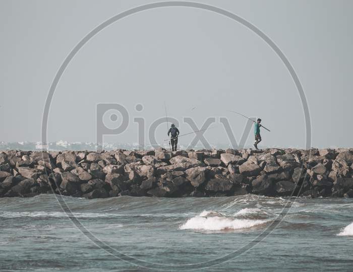 Kovalam, Tamil Nadu, India - February 04 2021: People Fishing Over The Rocks Along The Kovalam Beach, Chennai, India.