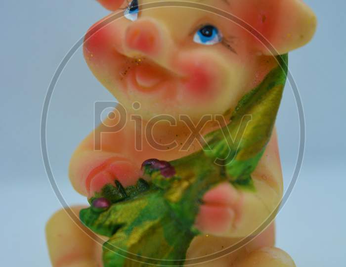 A bright colorful figurine of a pink pig in a red Christmas hat with a green Christmas tree is located on a white matte background.