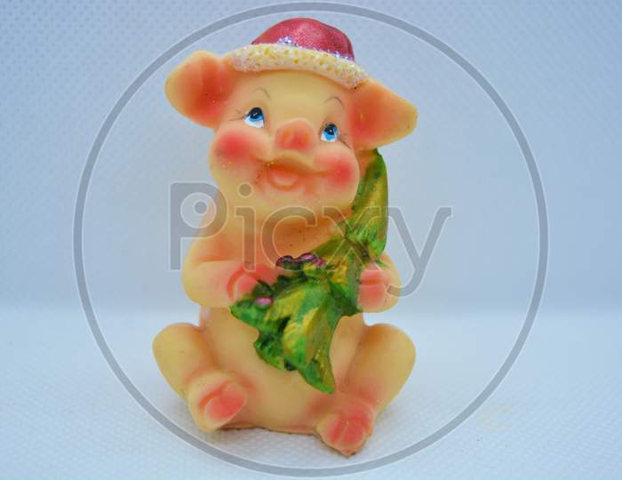 A bright colorful figurine of a pink pig in a red Christmas hat with a green Christmas tree is located on a white matte background.