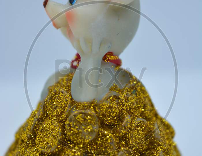 A figurine of a cute gray mouse peeking out of a mountain of yellow coins is located on a white fabric background.