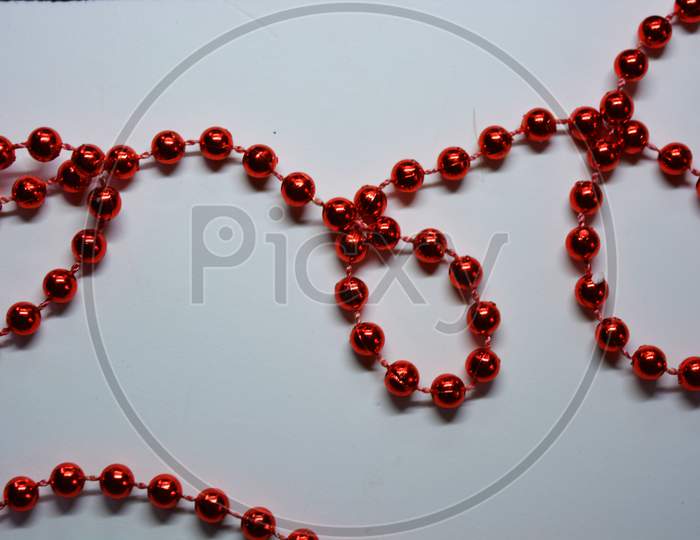 New Year's and Christmas red beads for the New Year tree are randomly scattered on a white fabric background.